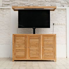 a flat screen tv sitting on top of a wooden cabinet next to a brick wall