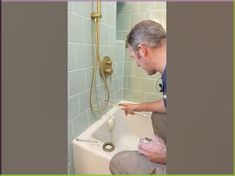 a man sitting on the edge of a bathtub in front of a shower head