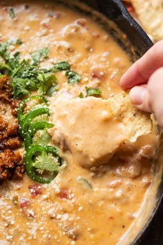 a hand dipping some food into a bowl with tortilla chips on the side