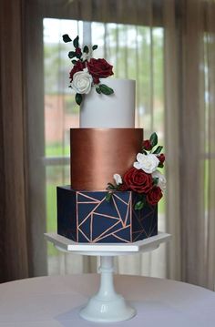 a three tiered cake with red and white flowers on top sits on a table