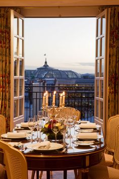 a dining room table is set with place settings and candles in front of an open window