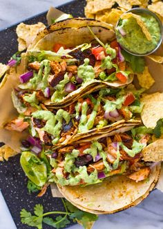 three tortillas with guacamole and salsa on a black plate next to chips