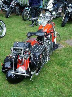 an orange motorcycle parked on top of a lush green field next to other motorcyclists