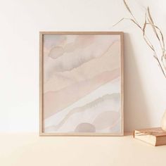 a white vase sitting on top of a table next to a framed painting and a book