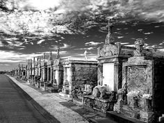 black and white photograph of many headstones on the side of a road with clouds in the sky