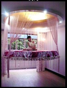 a woman sitting on top of a bed in a room with pink curtains and drapes