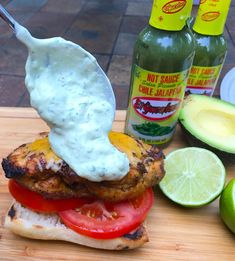 a chicken sandwich with ranch dressing on top and sliced avocado, tomatoes, and limes