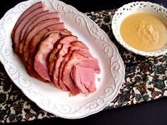 slices of ham on a white plate next to a bowl of mustard