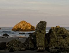 some rocks on the beach and one large rock in the water