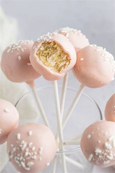 some pink cake pops with white sprinkles in a clear glass bowl on a table