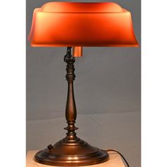 a lamp that is sitting on top of a wooden base with a red shade over it