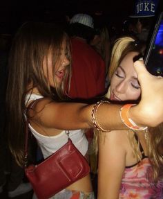 two young women taking pictures with their cell phones at a party in the night time