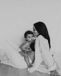 a black and white photo of a woman holding a baby in her lap while sitting on the floor