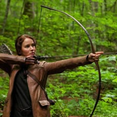 a woman in the woods shooting an arrow