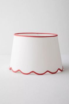 a white lamp shade with red trim on the bottom and side, against a white background