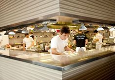 a man standing in a kitchen preparing food on top of a counter next to other people