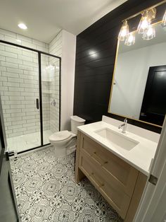 a white toilet sitting next to a walk in shower under a bathroom mirror above a sink