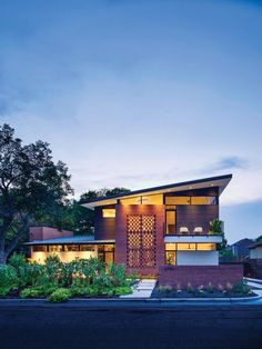 a modern house is lit up at night with the lights on and plants growing in front