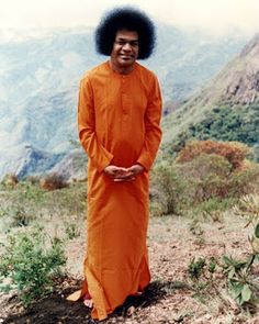 a man in an orange outfit standing on top of a hill with mountains in the background