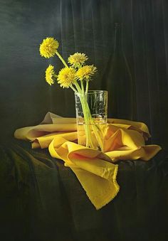 a glass vase filled with yellow flowers sitting on top of a cloth covered tablecloth