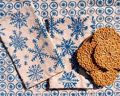 two napkins with blue snowflakes on them sitting next to each other in front of a white and blue table cloth