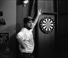 a man standing in front of a dartboard holding his hand up to the air