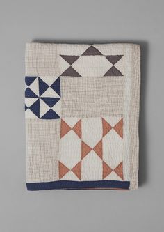 a white and blue quilt on top of a gray surface with an orange, black, and grey geometric design