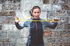 a woman holding two yellow hula hoops in front of her face while standing next to a brick wall