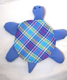 a stuffed turtle is laying on a white sheet with blue and green plaid around it's neck