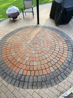 a brick patio with chairs and an umbrella in the back ground, next to a grill