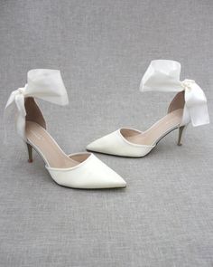 a pair of white high heel shoes with bows on the toe and heels are shown