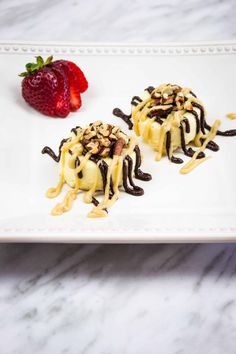 two desserts on a white plate topped with chocolate, nuts and a strawberries