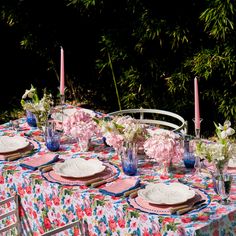 the table is set with pink and white flowers, blue glassware, and candles