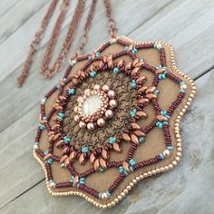 SOUTHWESTERN BLOOM This light weight pendant is big, bold and beautiful. Hand-stitched and beaded with multiple types of glass beads, the pendant has shades of copper and rose gold that surround copper filigree and a focal crystal. Bright turquoise beads and crystals add contrast and sparkle to the mandala. The chain is 30 inches long, and The pendant's back is made of soft ultra suede, which is comfortable to wear against the skin. OVERVIEW * CHAIN LENGTH: 30 inch chain, no clasp * PENDANT DIMENSIONS: 3 1/4 inches wide; 3 1/2 inches long TECHNIQUES--The pendant was handmade using bead embroidery, a sewing and beadwork technique that uses a needle and thread to sew beading to a foundation that is then backed in ultra suede.  MATERIALS * Crystal rivoli  * Japanese seed beads * Copper-plated Artisan Hand-stitched Festival Jewelry, Artisan Beaded Necklace With Large Pendant, Beaded Mandala, Long Statement Necklace, Bead Embroidery Patterns, Bright Turquoise, Jewelry Crystal, Bold And Beautiful, Geometric Jewelry