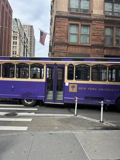 a purple and yellow bus parked in front of a tall building on a city street