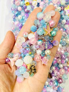 a hand holding a bunch of different colored beads in it's palm, next to a pile of shells and seashells