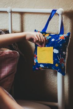 a person sitting on a bed with a blue and yellow bag hanging from it's side