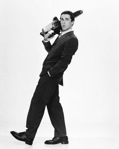 a man in a suit and tie holding a camera up to his head while standing against a white background