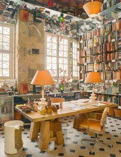 a room filled with lots of books on top of a wooden table next to two lamps