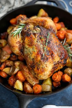 a close up of a chicken in a pan with potatoes and carrots on the side