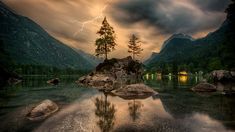 a lake with rocks and trees in the foreground as a lightning strikes over it