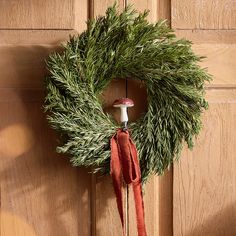 a wreath hanging on a door with a red ribbon around it and a mushroom in the middle