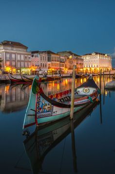 several boats are docked in the water near buildings and lights at night, along with another rowboat