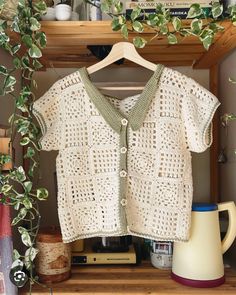 a crocheted shirt hanging on a shelf next to a coffee pot and mug