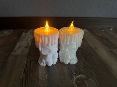 two white candles sitting on top of a wooden table next to each other with yellow lights