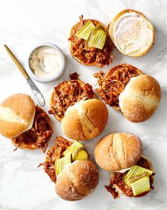 several pulled pork sandwiches with pickles and ranch dressing on a marble surface next to a knife