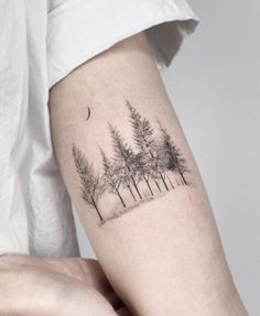 a person with a tattoo on their arm that has trees and a moon in the background