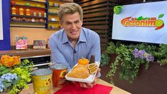 a man holding a tray with food on it in front of a tv screen and flowers