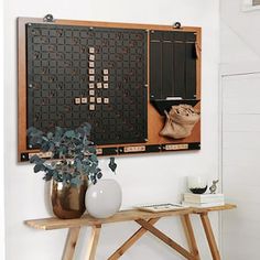 a wooden table topped with a vase filled with flowers next to a wall mounted scrabble board