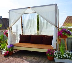 a white canopy bed sitting on top of a wooden deck next to potted plants